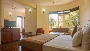 Habitación de hotel con cama, televisión, escritorio y ventana con vistas a árboles.