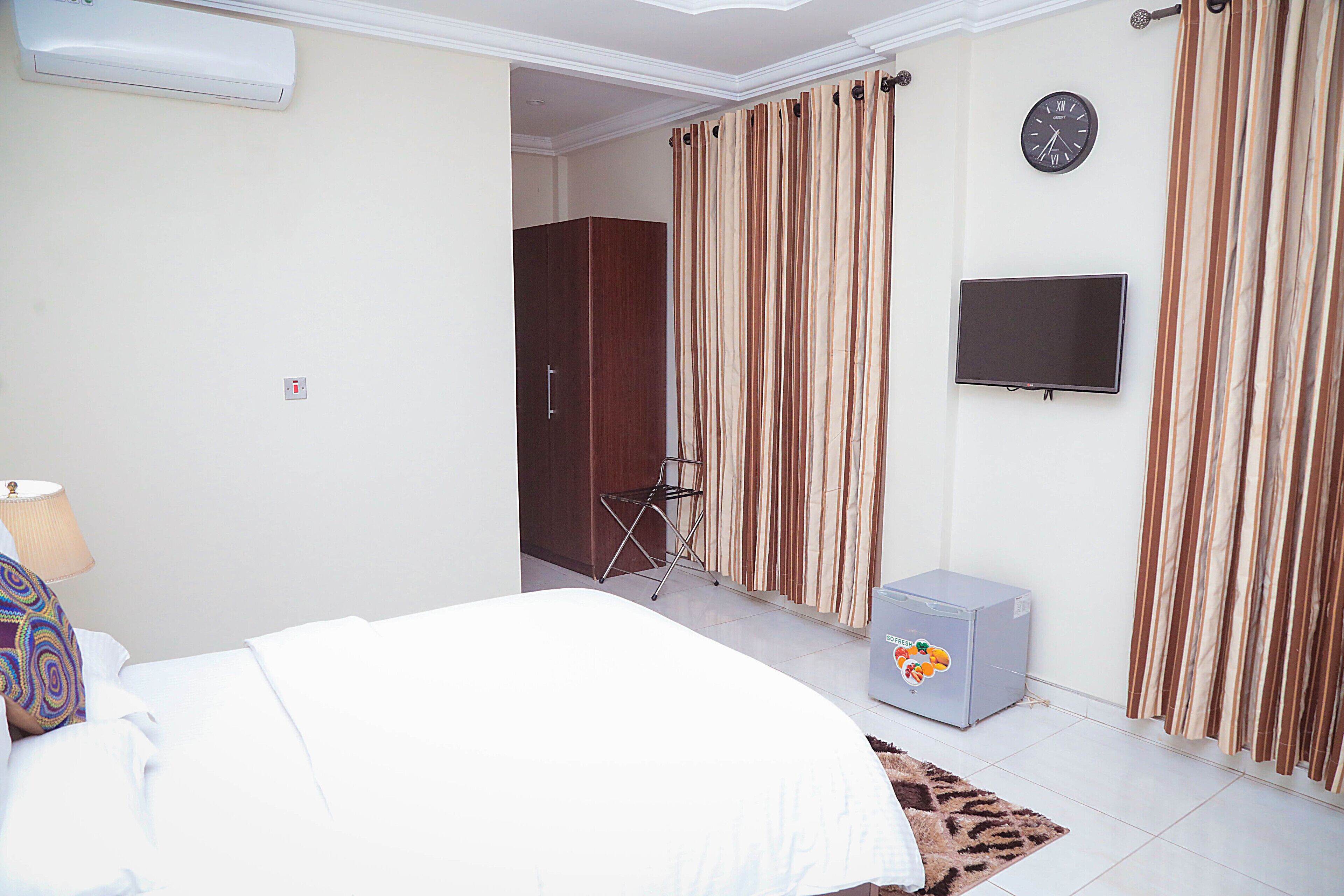 A hotel room with a bed, a TV, curtains, a wardrobe, and a small refrigerator.
