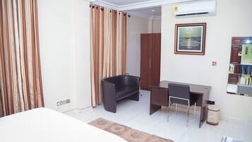 Habitación de hotel con una cama, un escritorio, una silla, un cubo de basura y un cuadro en la pared.