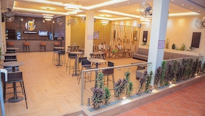 Un restaurante con zona de bar, varias opciones de asientos, incluyendo mesas y sillas, y una decoración vegetal a lo largo de la barandilla.