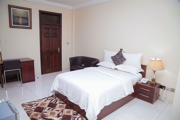 A neatly arranged bedroom with a bed, bedside table, lamp, and a framed quote on the wall.