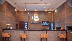 Un bar y restaurante con barra de mármol, cuatro taburetes, una pantalla de televisión e iluminación moderna.