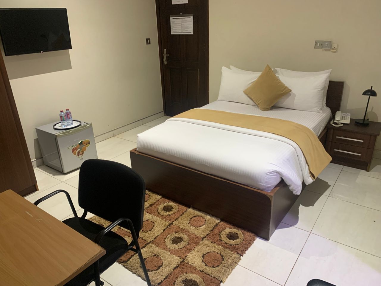 A hotel room with a bed, bedside table, chair, and a small desk with a chair.