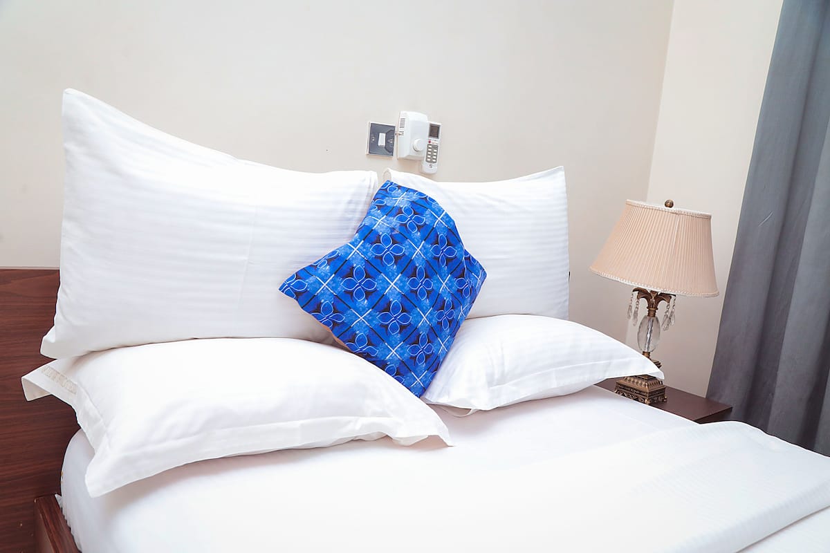 A neatly made bed with white pillows and a blue patterned pillow, a bedside lamp, and a small decorative item on the nightstand.
