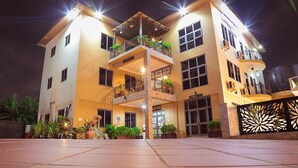 Un hotel de varios pisos con recepción en la planta baja, balcones con plantas y una entrada bien iluminada.
