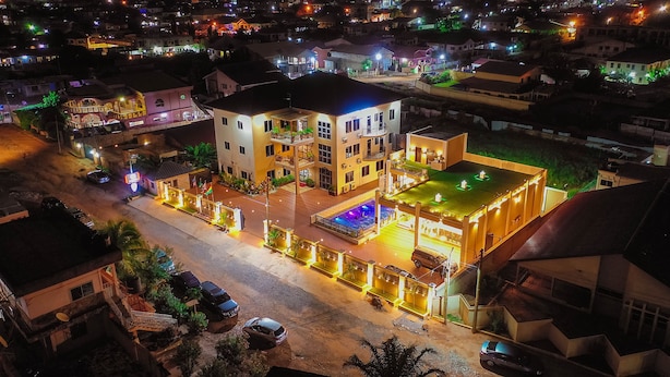 Un hotel de varios pisos con piscina en la azotea, rodeado de calles bien iluminadas y edificios cercanos.