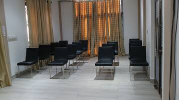 Um quarto com fileiras de cadeiras pretas organizadas para acomodação, um chão de azulejos claros e uma janela com cortinas.