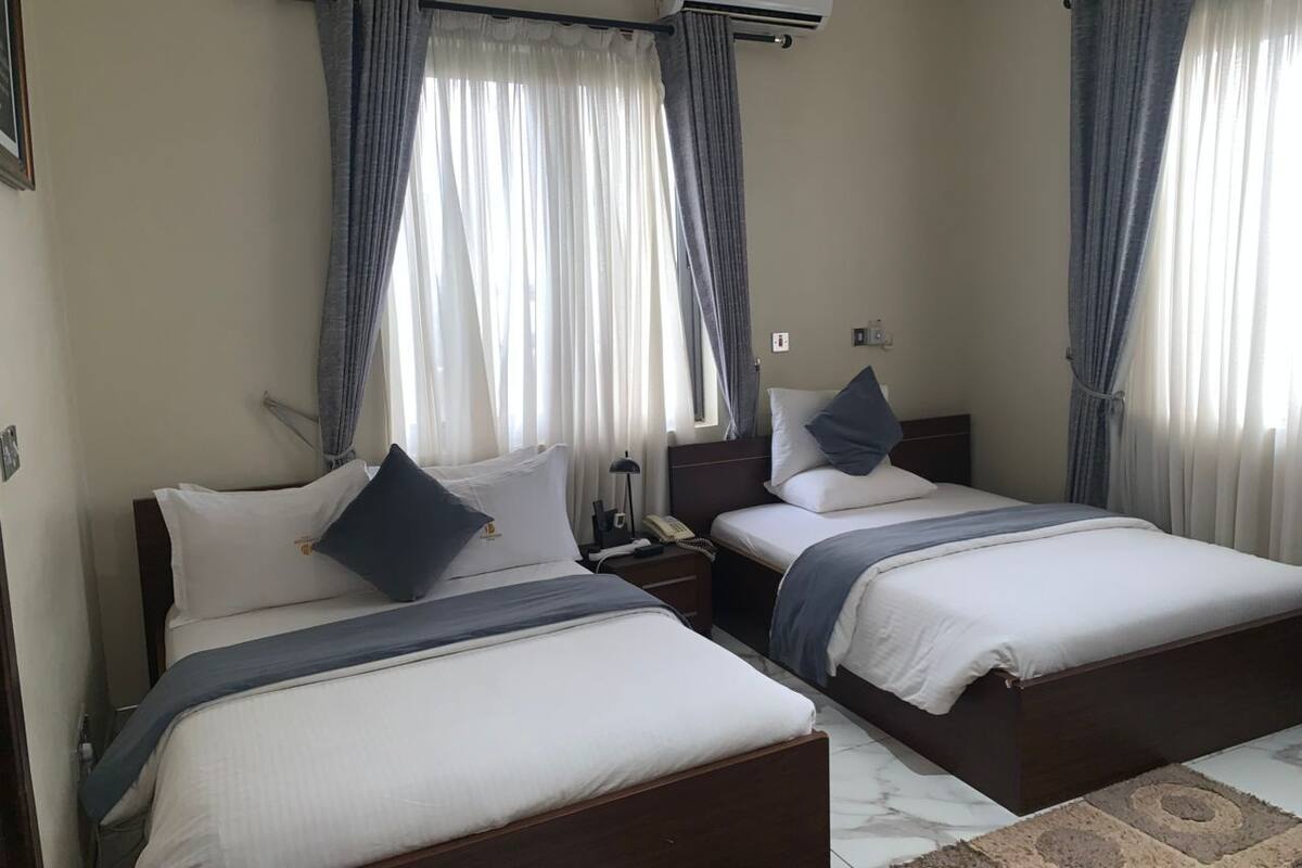 A hotel room with two beds, a nightstand, a lamp, and an air conditioning unit.