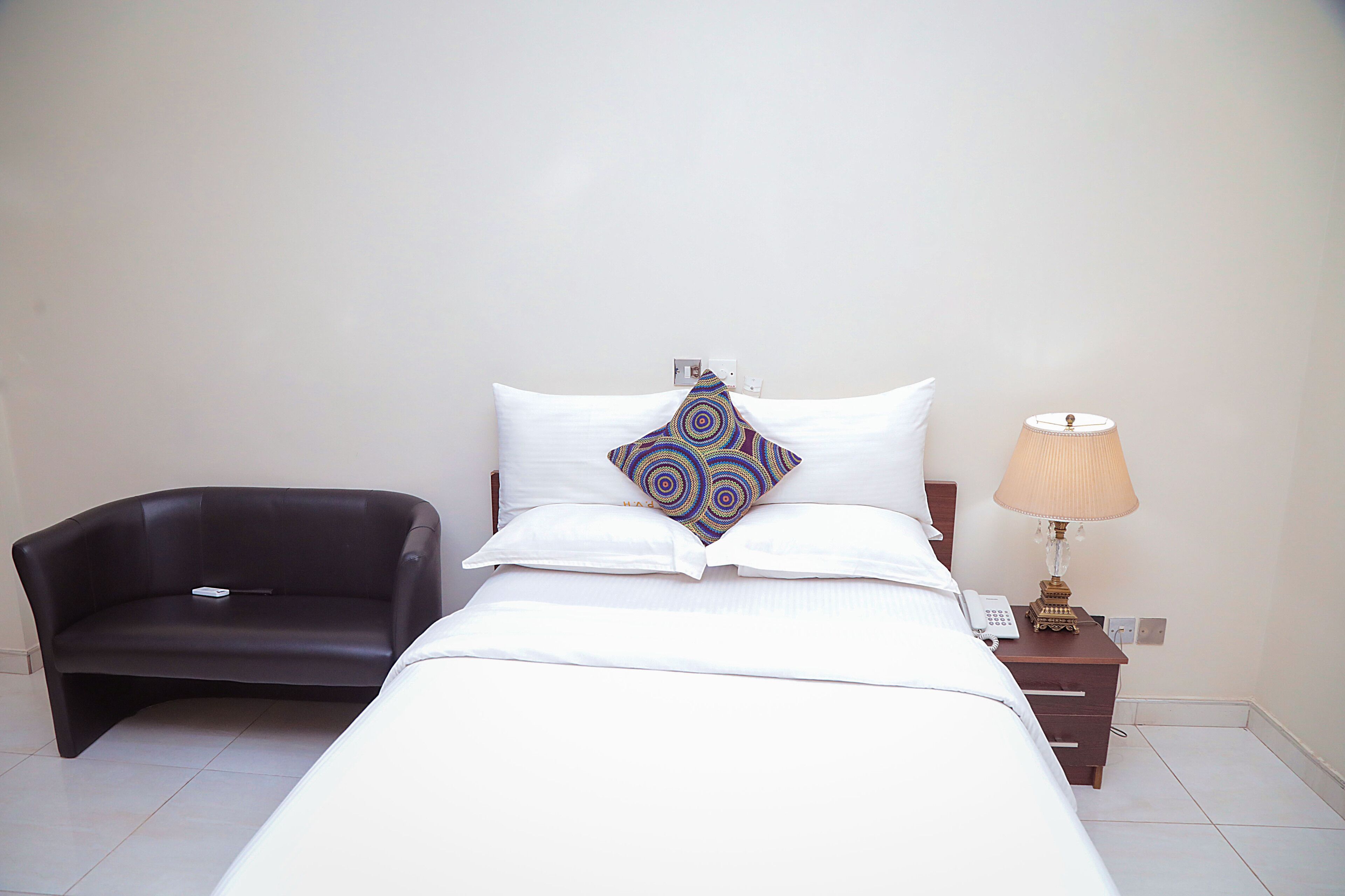 A neatly arranged hotel room with a bed, a bedside lamp, a small table, and a chair.