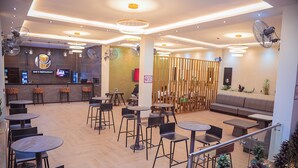 Un bar restaurante moderno con varias zonas de estar, incluyendo mesas y sillas redondas, una barra y un separador de madera.
