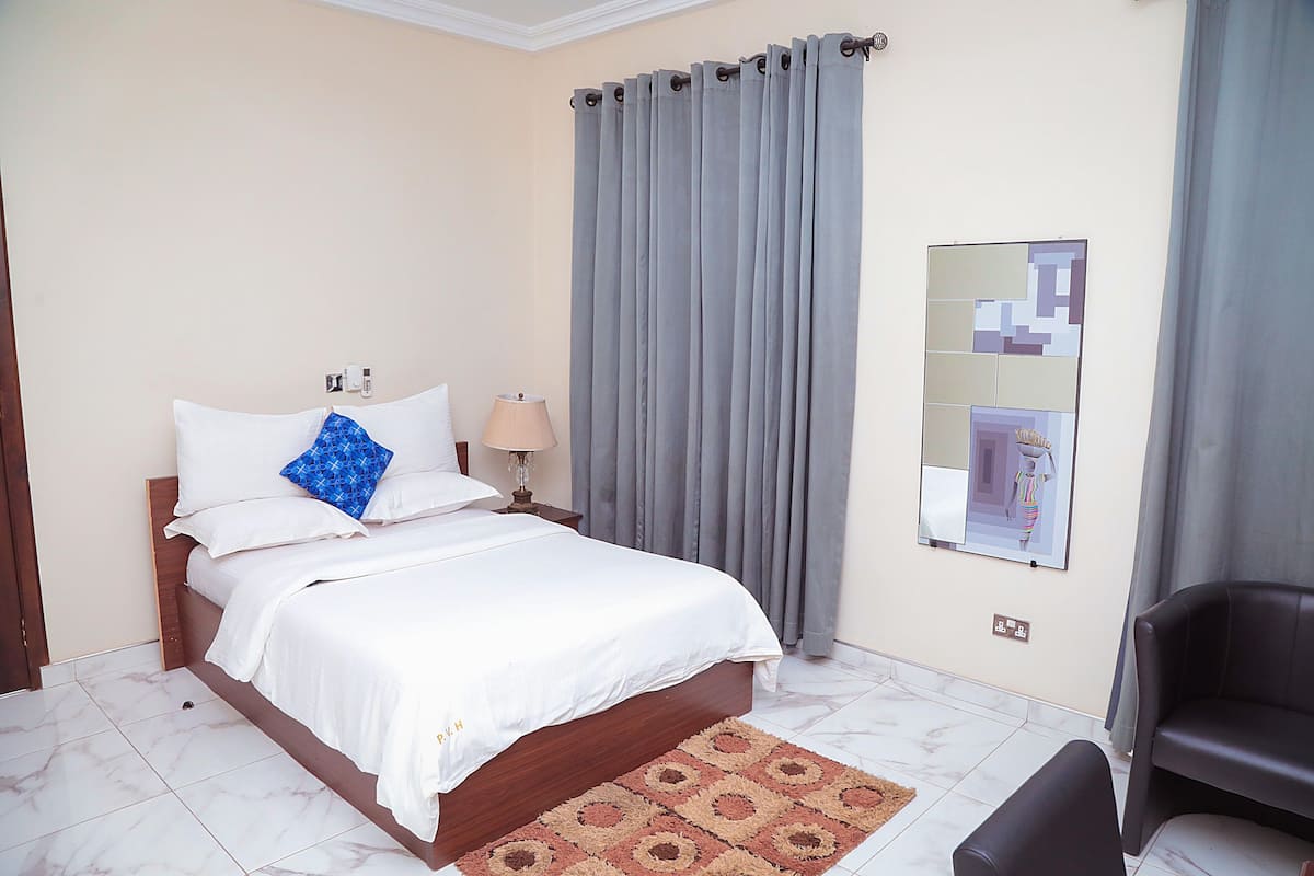 A hotel room with a bed, a nightstand, a lamp, a chair, and a wall-mounted mirror.