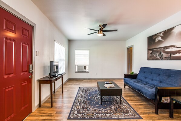 A living room with a red door, a ceiling fan, a blue sofa, a coffee table, and a large rug.