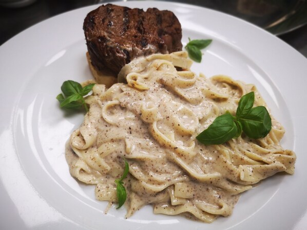 Un plato de pasta con bistec y hojas de albahaca.