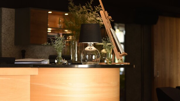A wooden reception desk with a lamp, a notebook, and decorative items.