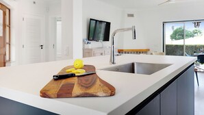 A modern kitchen with a large island, a built-in sink, and a wooden cutting board with lemon slices.