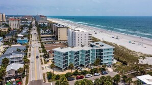 A coastal cityscape with a beachfront hotel featuring multiple floors, a parking lot, and a view of the ocean. - Sandpiper Oceanfront 5F (Jacksonville Beach)