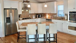 A modern kitchen with white cabinets, stainless steel appliances, a central island with bar stools, and pendant lighting. -  Cape May Beach- Luxury Delaware Bay Beauty- Heated Pool-Linens (Cape May Beach)