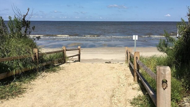 A sandy beach with a wooden fence leading to the water, a clear sky, and a calm sea. -  Cape May Beach- Luxury Delaware Bay Beauty- Heated Pool-Linens (Cape May Beach)