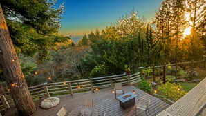 Una terraza de madera con mobiliario exterior, un hogar y luces colgantes.