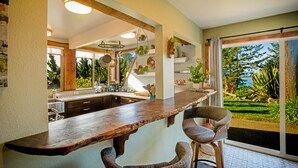 Una cocina con encimera de madera, dos taburetes de bar y vistas a un jardín a través de un ventanal corredero.