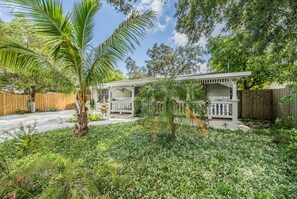 A two-story house with a covered porch, surrounded by lush greenery and a wooden fence. - #1 LOCATION - Walk to Amusement Parks from PERFECT HOME, Great for Families 🏠 (Tampa)