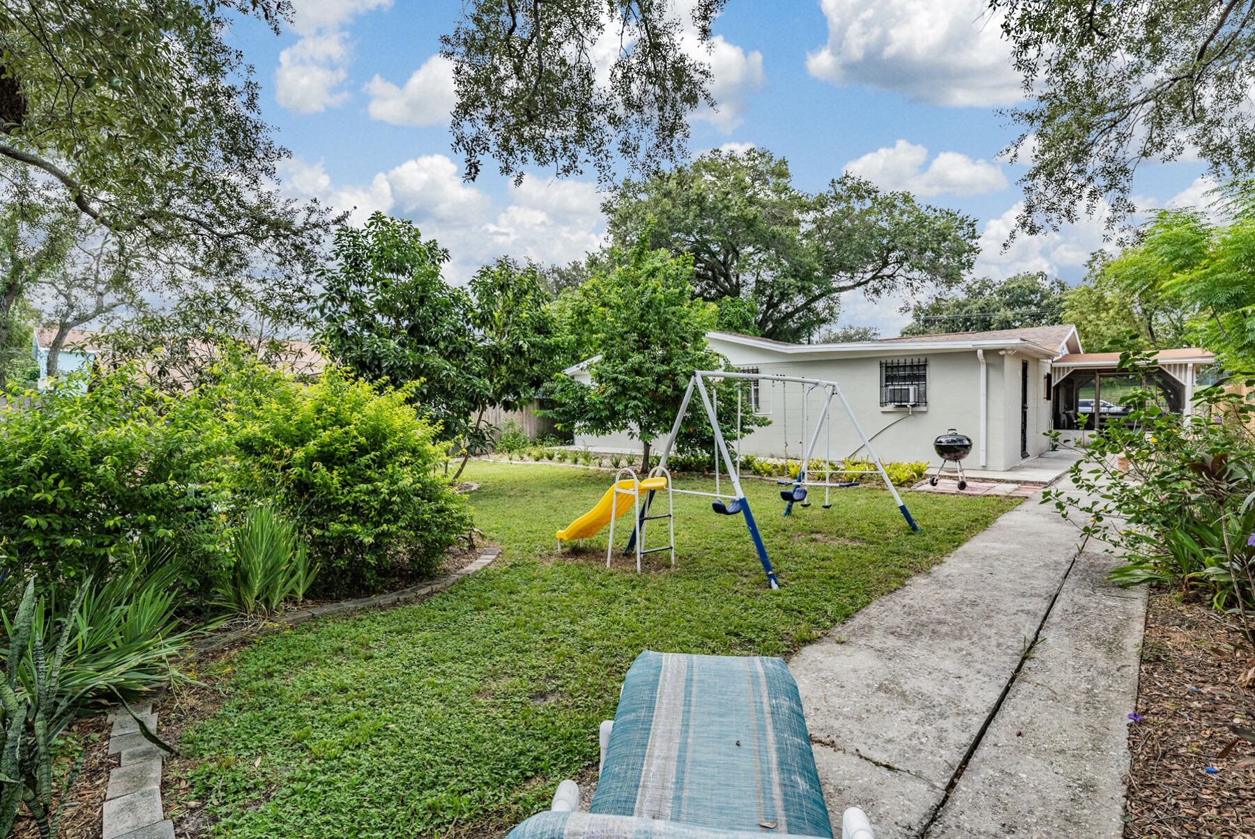 A residential backyard with a swing set, a slide, and a barbecue grill.