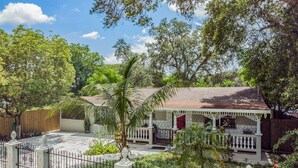 A house with a porch, surrounded by a fence and lush greenery. - #1 LOCATION  - Walk to Amusement Parks from PERFECT HOME, Great for Families 🏠 (Tampa)