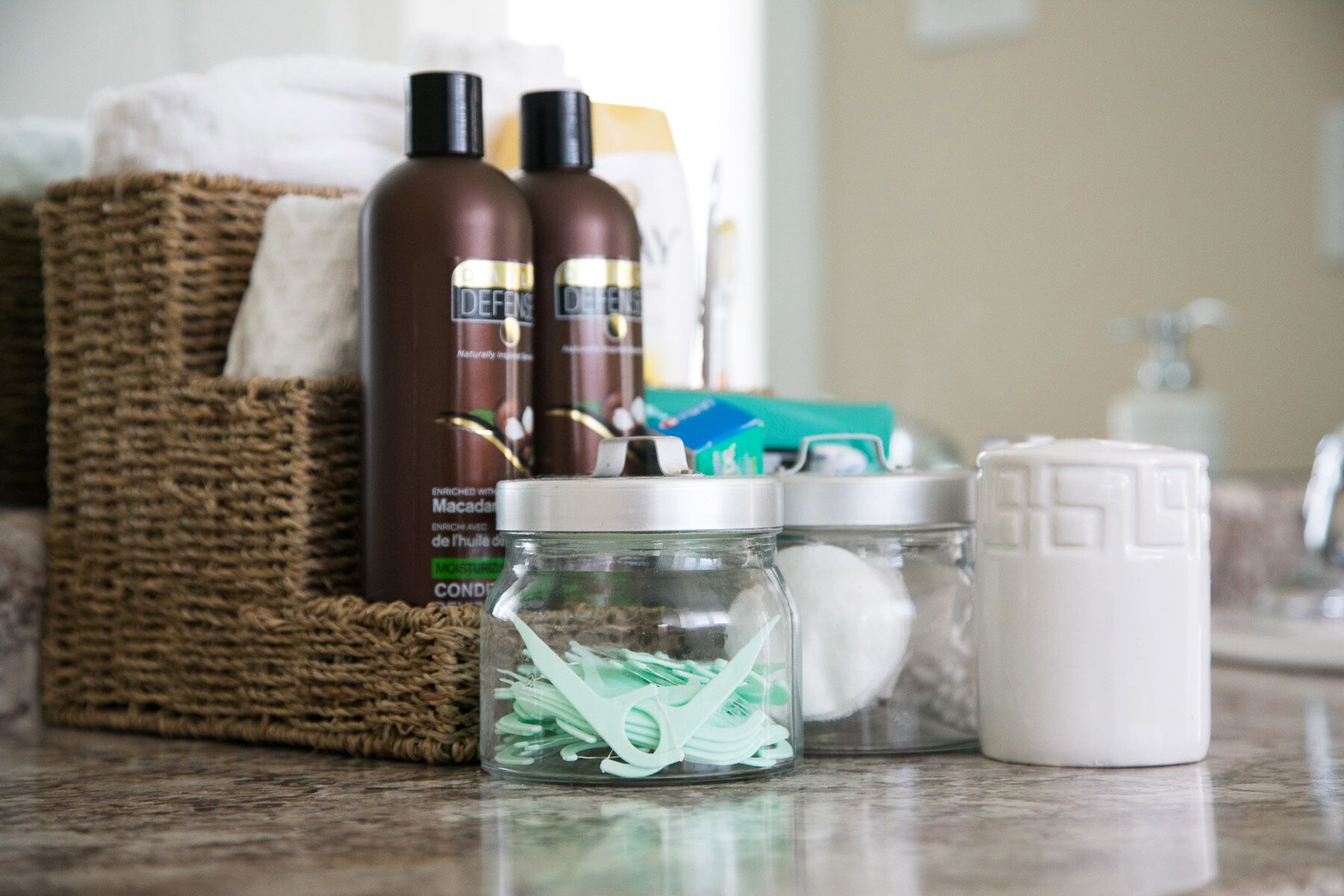 A bathroom counter with toiletries, a wicker basket, and a glass jar with green items.