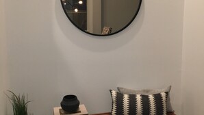 A round mirror on a wall, a wooden bench with a patterned pillow, and a potted plant beside the bench. - Monthly  1 Story, 3 Bdr Gorgeous Home Summerlin Pet Friendly (Las Vegas)