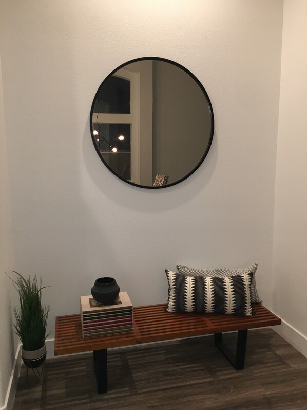 A round mirror on a wall, a wooden bench with a patterned pillow, and a potted plant beside the bench. - Monthly 1 Story, 3 Bdr Gorgeous Home Summerlin Pet Friendly (Las Vegas)