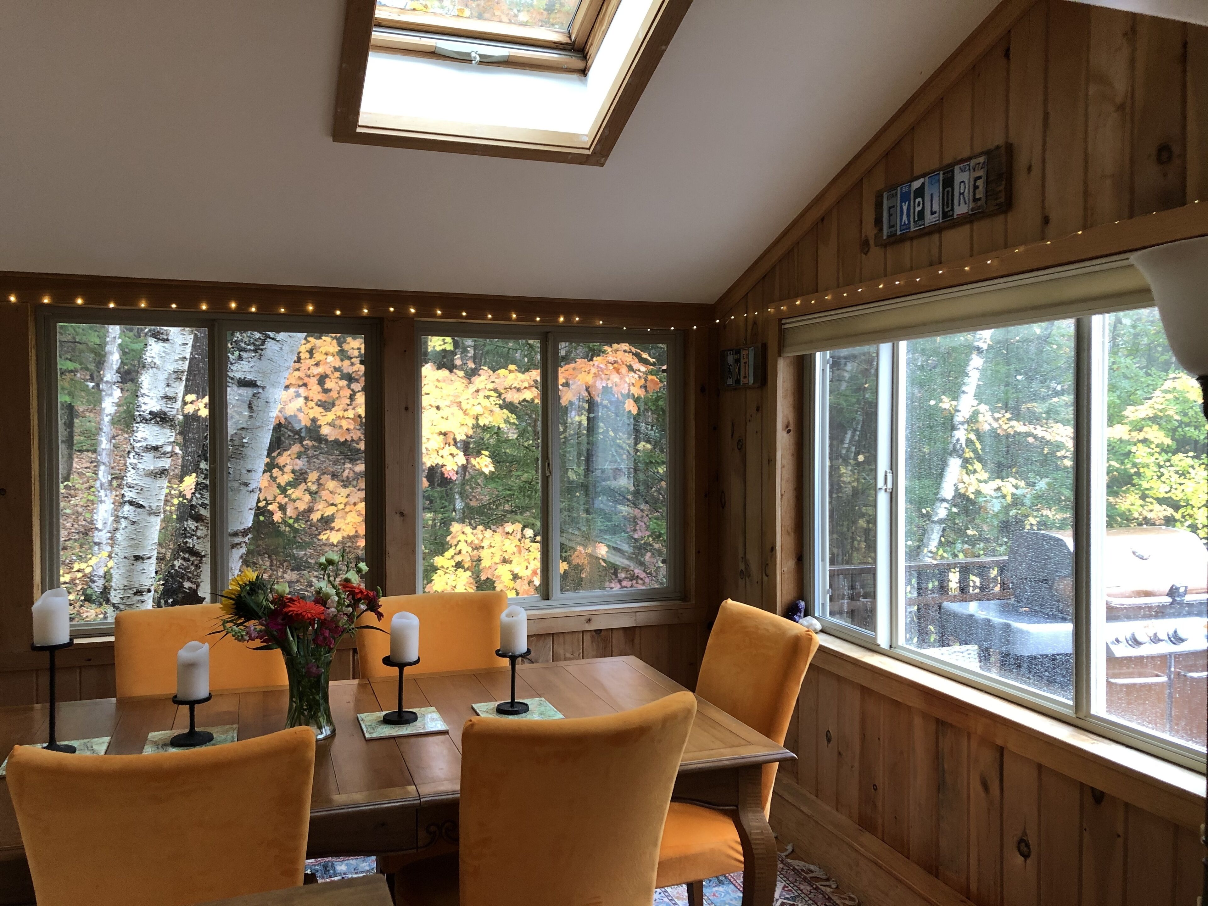 Ein Essbereich mit Holztisch und Stühlen, großen Fenstern mit Blick auf Herbstlaub und einem Oberlicht.