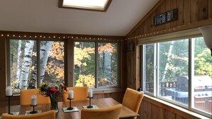 A dining area with a wooden table and chairs, large windows with autumn foliage views, and a skylight. - EPIC Mountain View Home : Minutes to Skiing!! (Jackson)