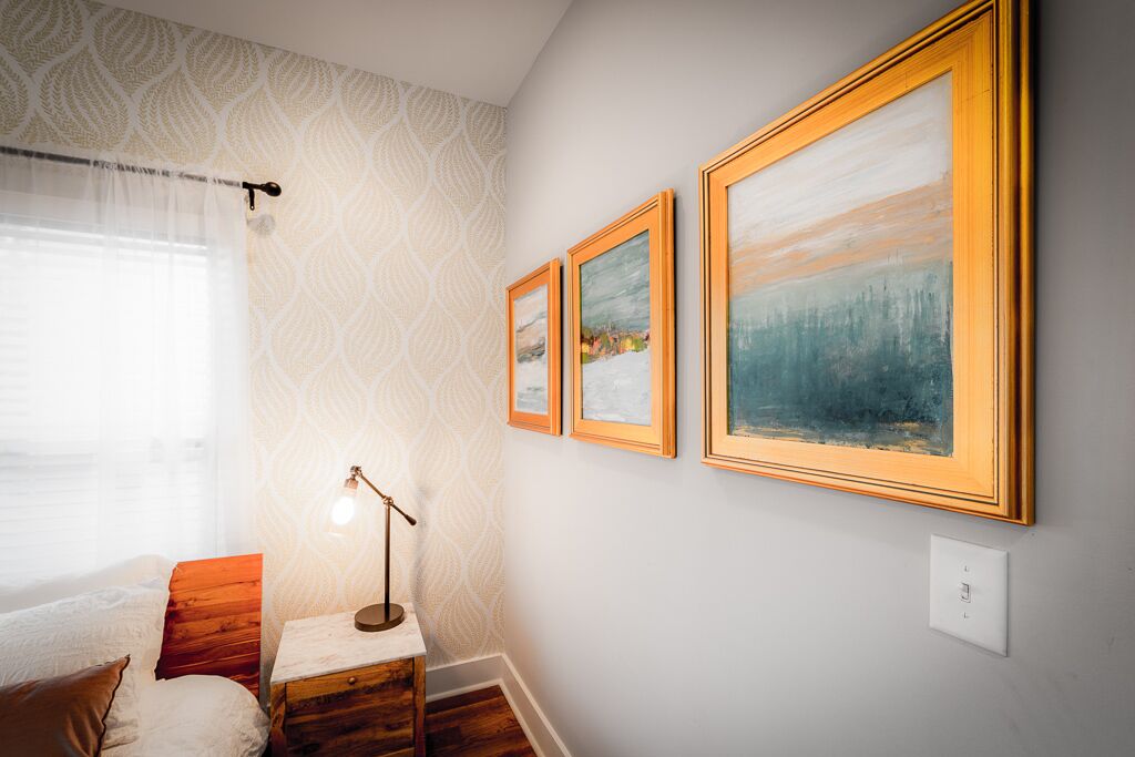 A bedroom with a bed, a nightstand, a lamp, and three framed paintings on the wall.