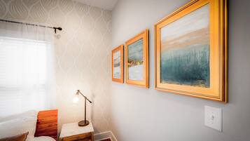 A bedroom with a bed, a nightstand, a lamp, and three framed paintings on the wall.