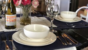 A dining table with a bottle of wine, a vase of flowers, and white dinnerware.
