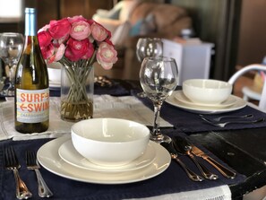 Una mesa de comedor con una botella de vino, un florero y vajilla blanca.