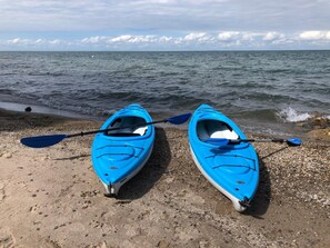 Dos kayaks sobre una playa pedregosa, con el mar al fondo.