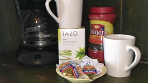 A coffee maker, a Tazo tea box, Folgers instant coffee, and two mugs on a wooden surface.