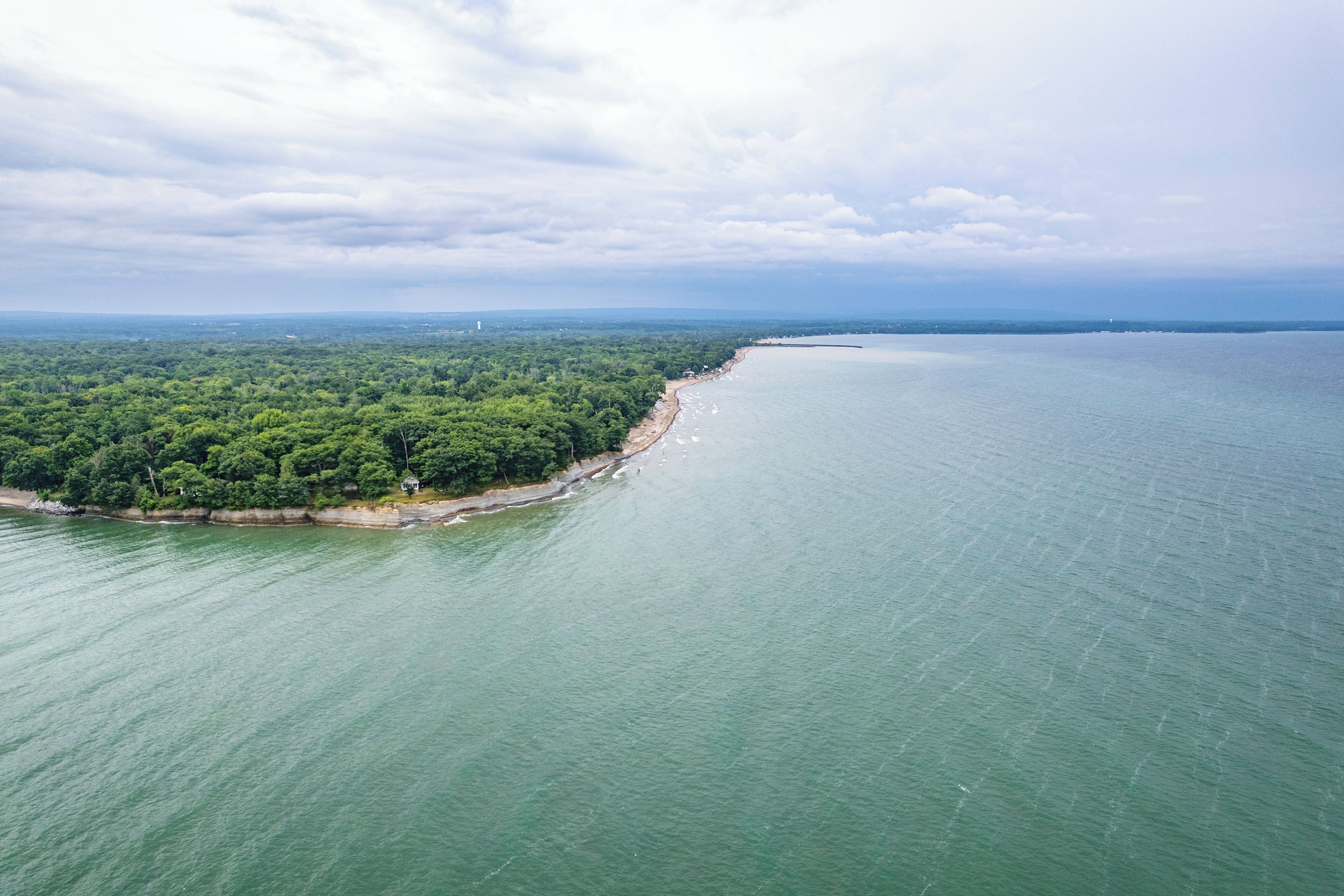 A coastal landscape with a beach, dense greenery, and a calm sea.