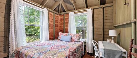 A cozy room with a bed, a table, and two windows.
