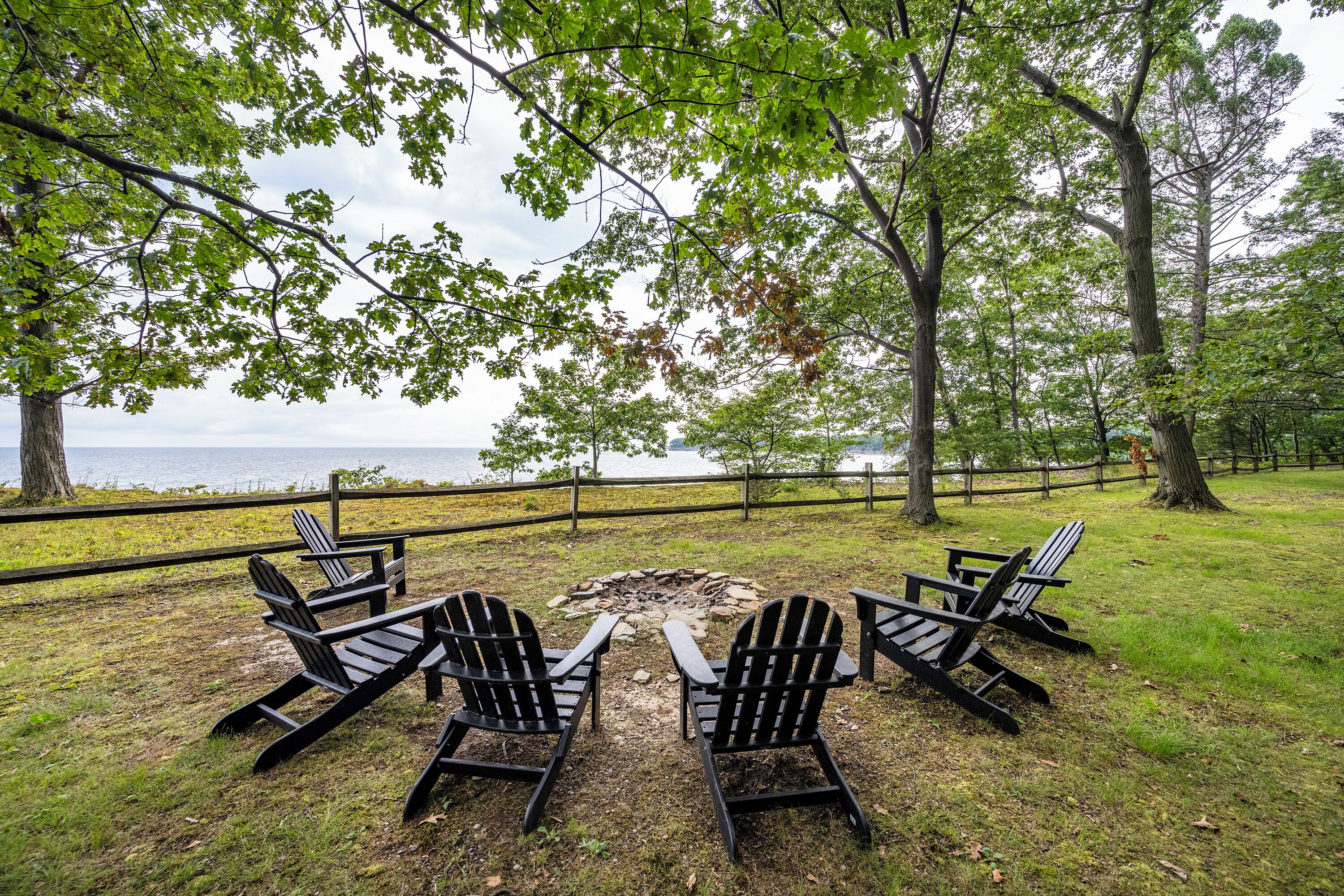 An outdoor seating area with Adirondack chairs around a fire pit, overlooking a body of water.