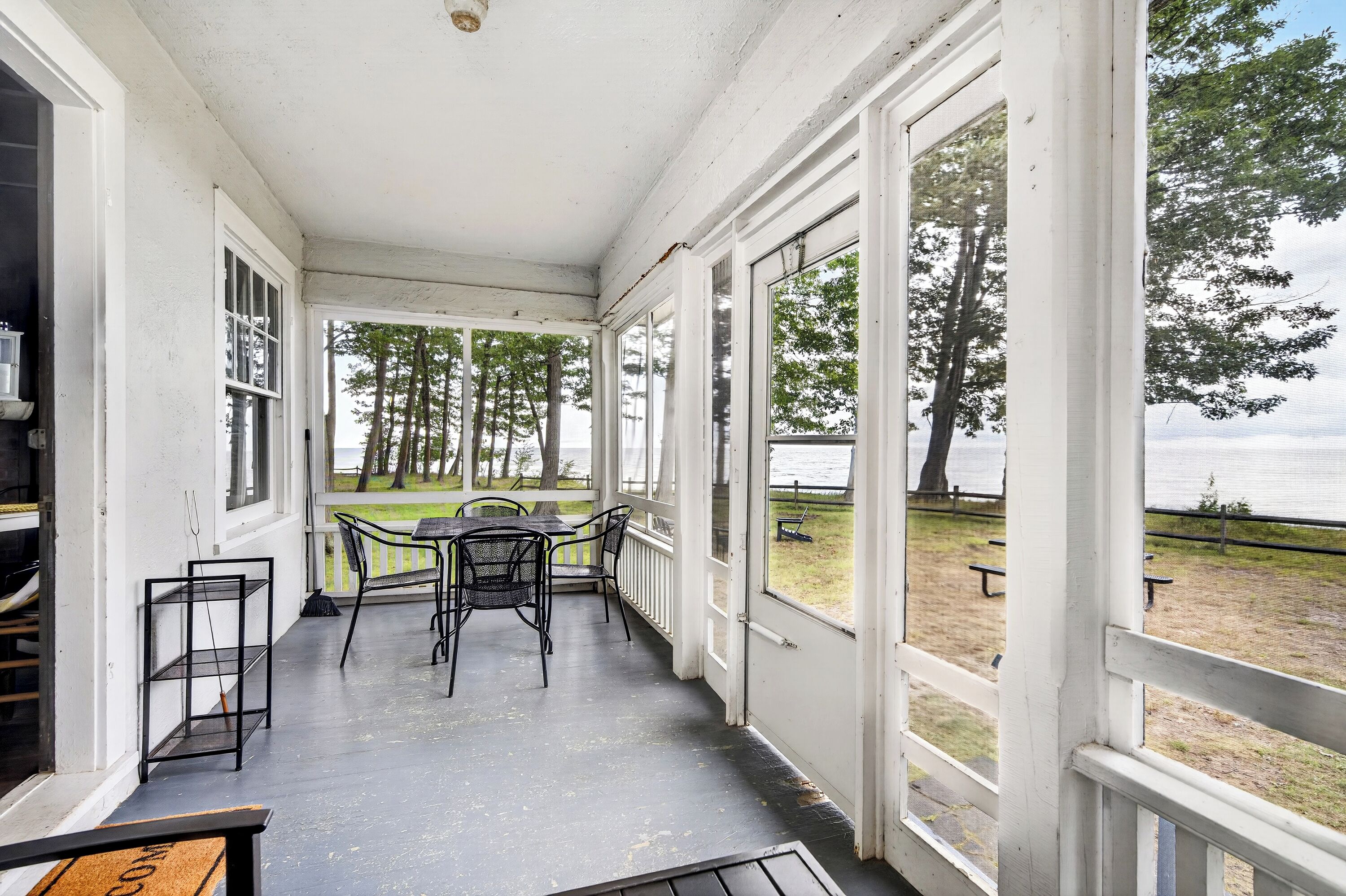 Une véranda avec une table et des chaises, de grandes fenêtres et une vue sur un parc.