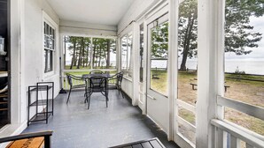 A covered porch with a table and chairs, large windows, and a view of a park. - "The Ellen" Beach Cottage, Wifi, Sleeps 6, All Seasons, 60-Acre Estate Access (Irving)