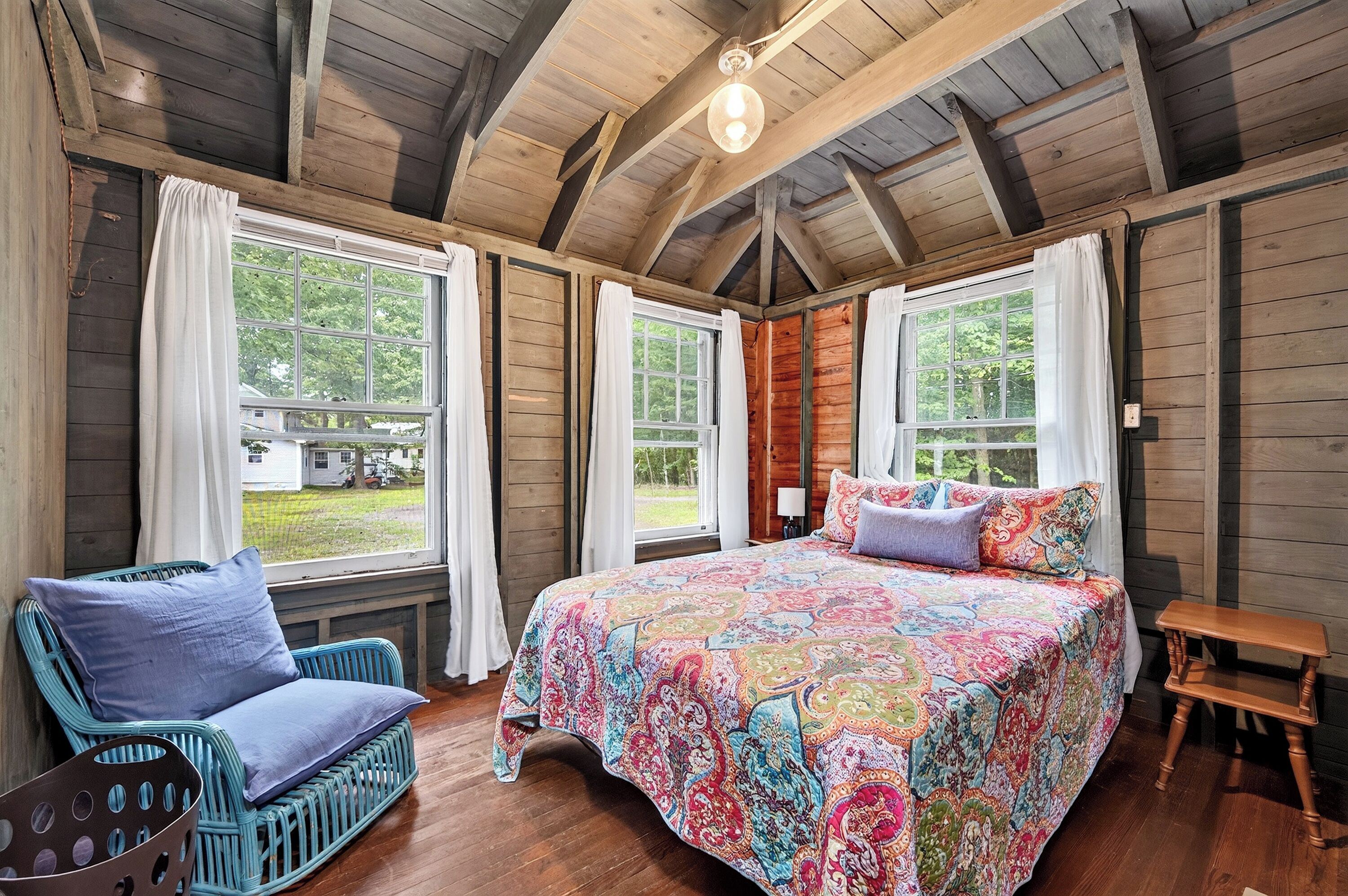 Une pièce de cabane en bois comprenant un grand lit, deux fenêtres, une chaise et une petite table.