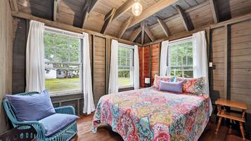 Une pièce de cabane en bois comprenant un grand lit, deux fenêtres, une chaise et une petite table.