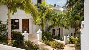 A white building with a covered outdoor area, palm trees, and a garden with various plants. - Villa Primavera | Oceanfront romantic getaway in Rincon (Rincón)