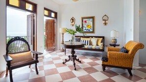 A spacious room with a checkered floor, a large fan, a sofa, a chair, and a table with a vase of plants. - Villa Primavera | Oceanfront romantic getaway in Rincon (Rincón)