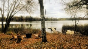 Une scène au bord d’un lac, avec un quai, des chaises et un bouleau.
