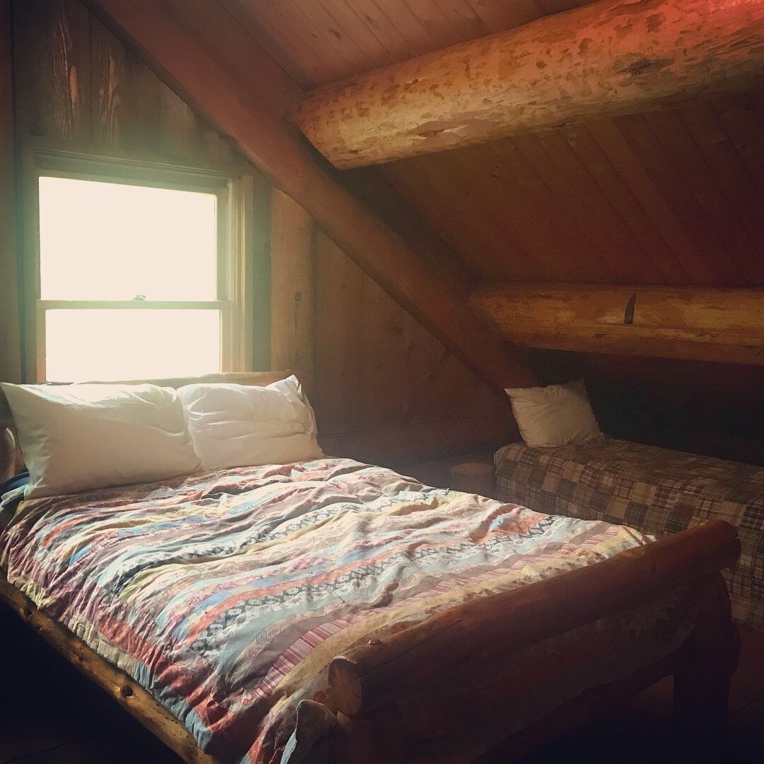 Een knus slaapkamer op zolder met een houten schuine dak en een groot raam dat natuurlijk licht biedt, en een bed met een kleurrijke quilt.