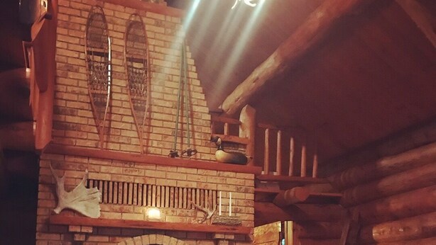 L’intérieur d’une cabane en rondins, avec une cheminée en briques, un plancher en bois et un tapis à motifs.